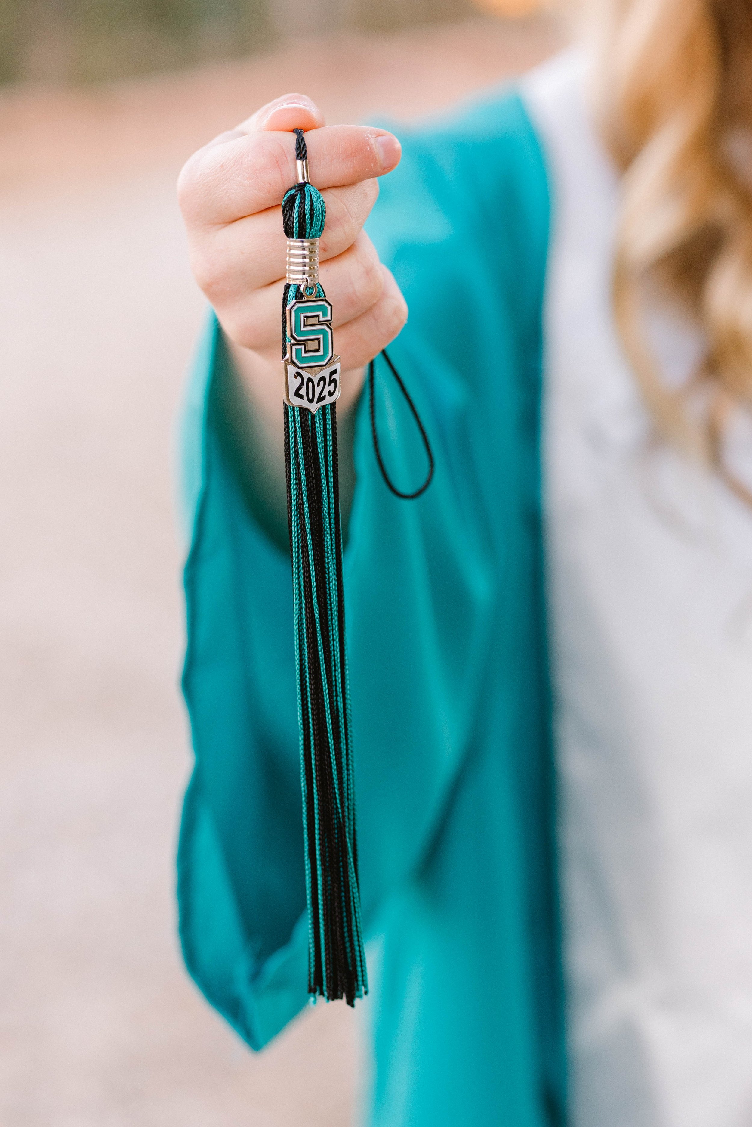 Person holding a graduate tassel with a school emblem, year 2025, and the letter S, wearing a blue jacket.