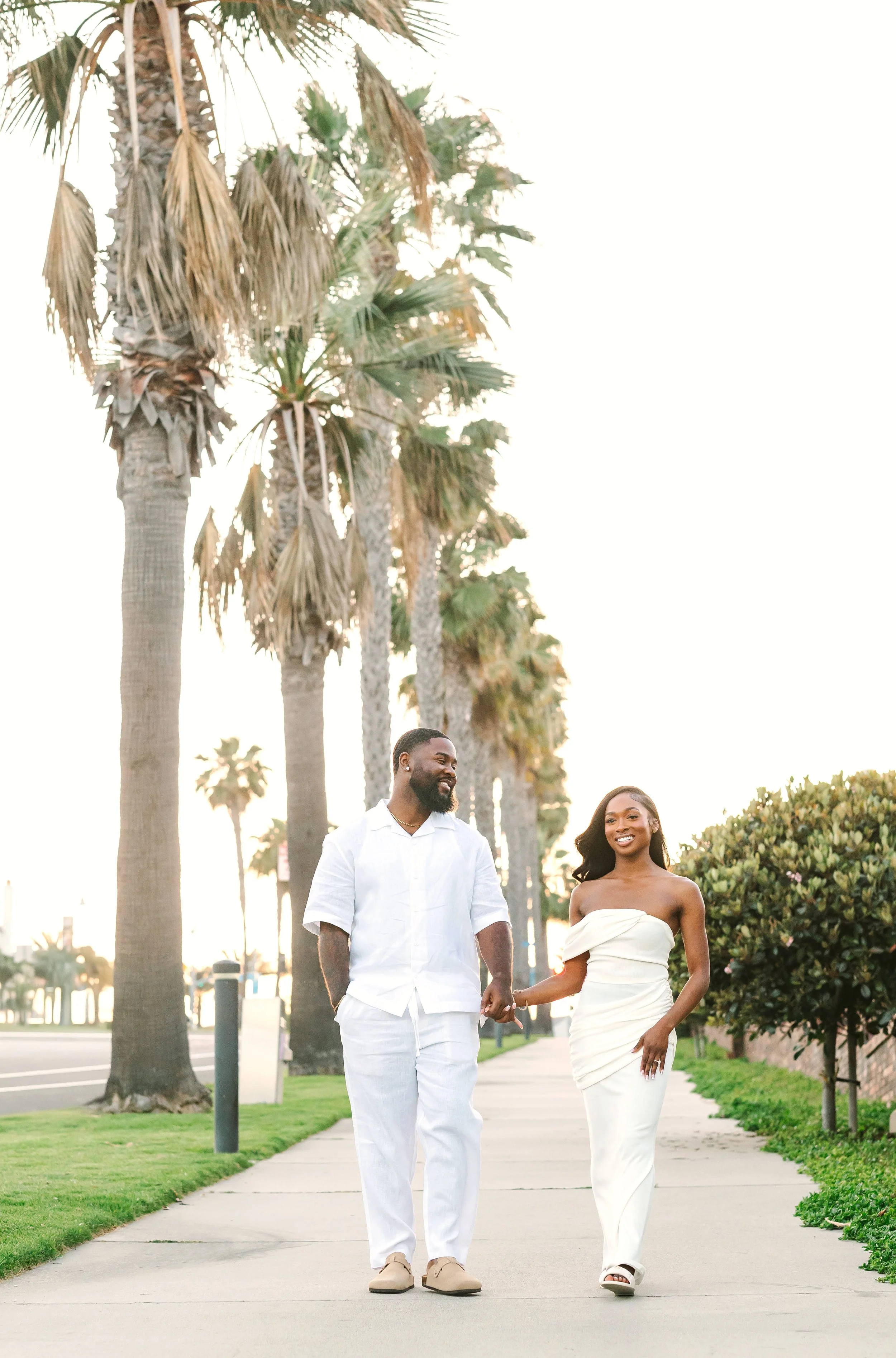Couple strolls hand in hand along palm tree lined road, Dana Point, California