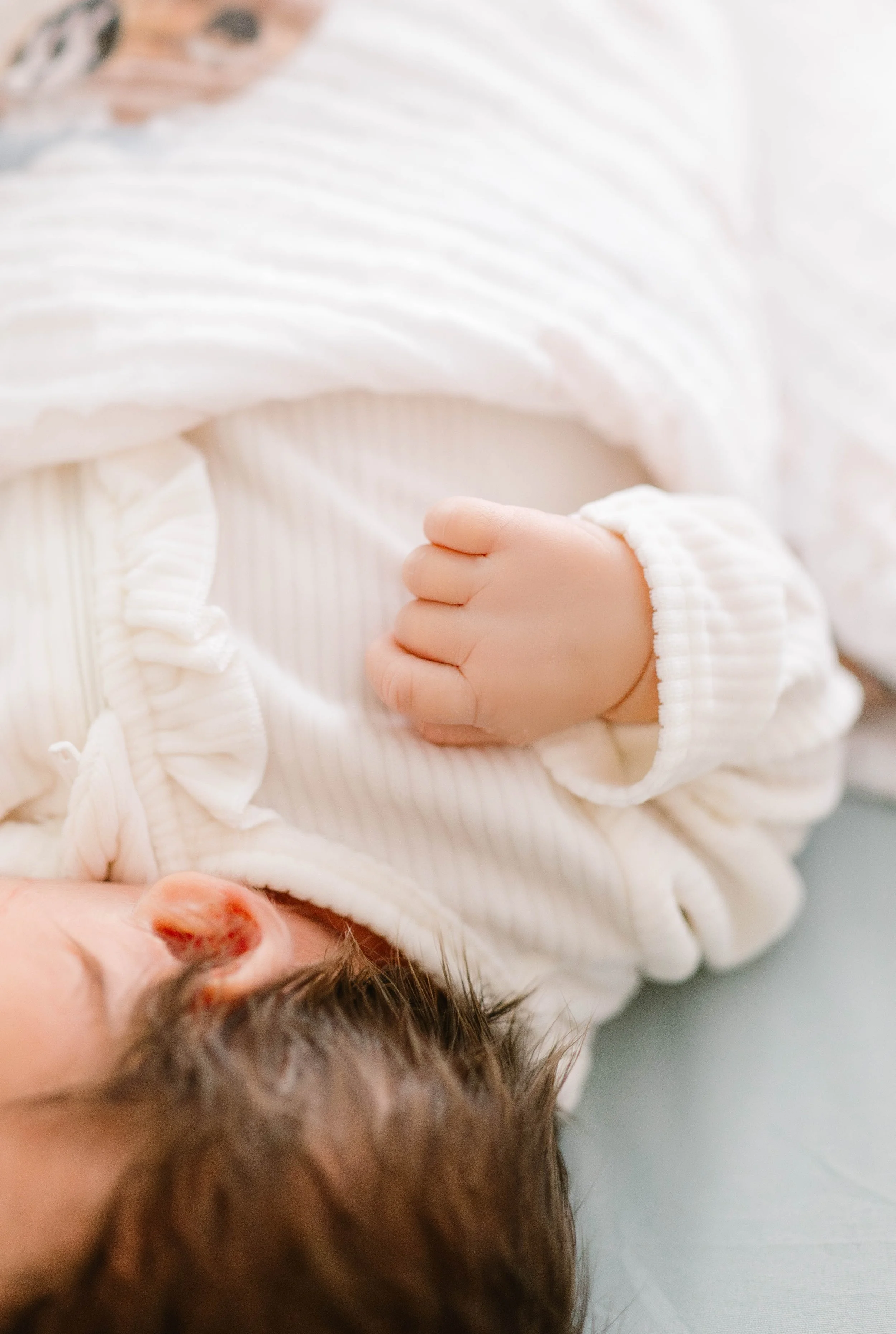 Close-up of a sleeping baby's hand resting on their chest, wearing a white, textured, long-sleeve onesie.