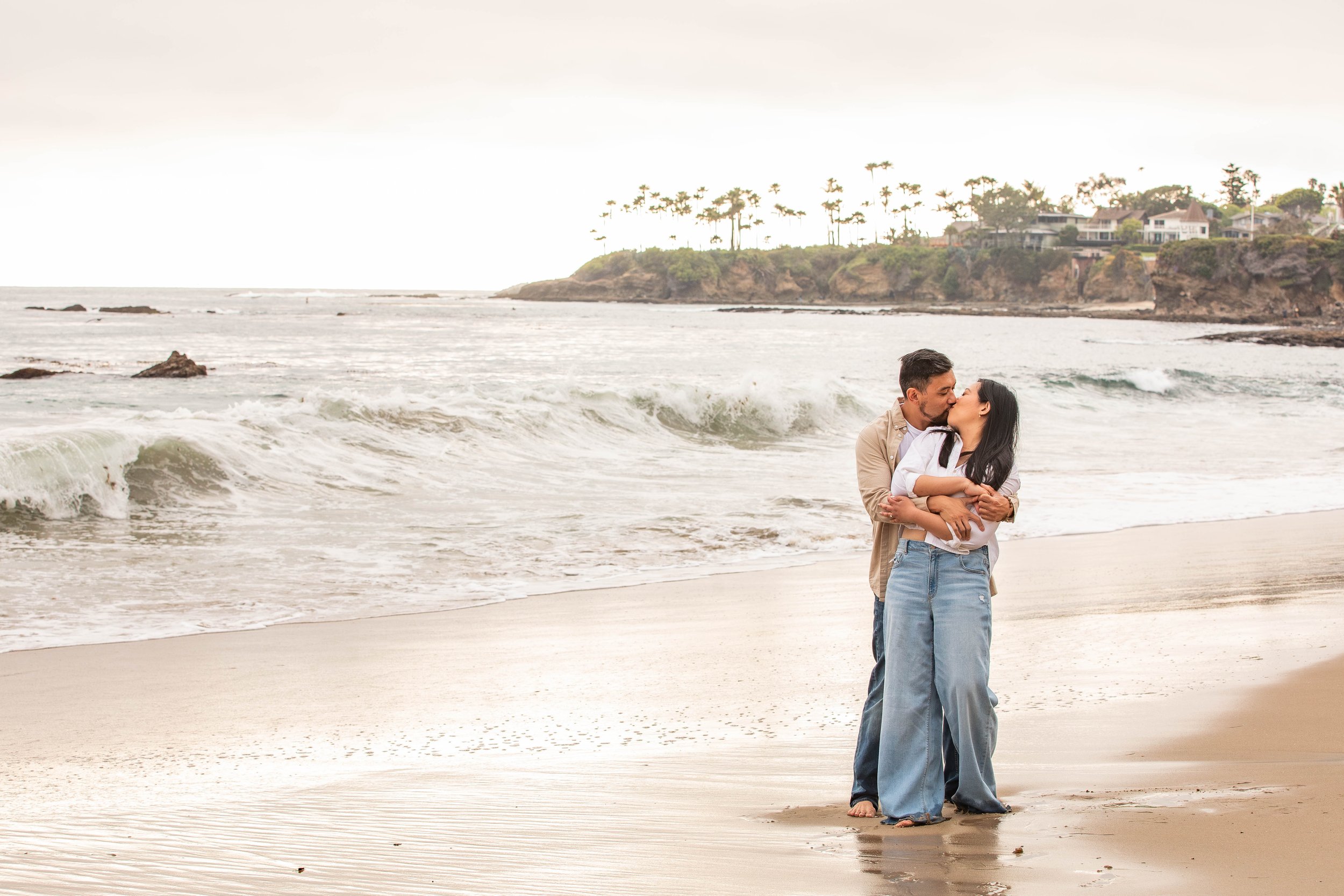 Couple embrace and kiss on the sand at the beach surrounded by cliffs
