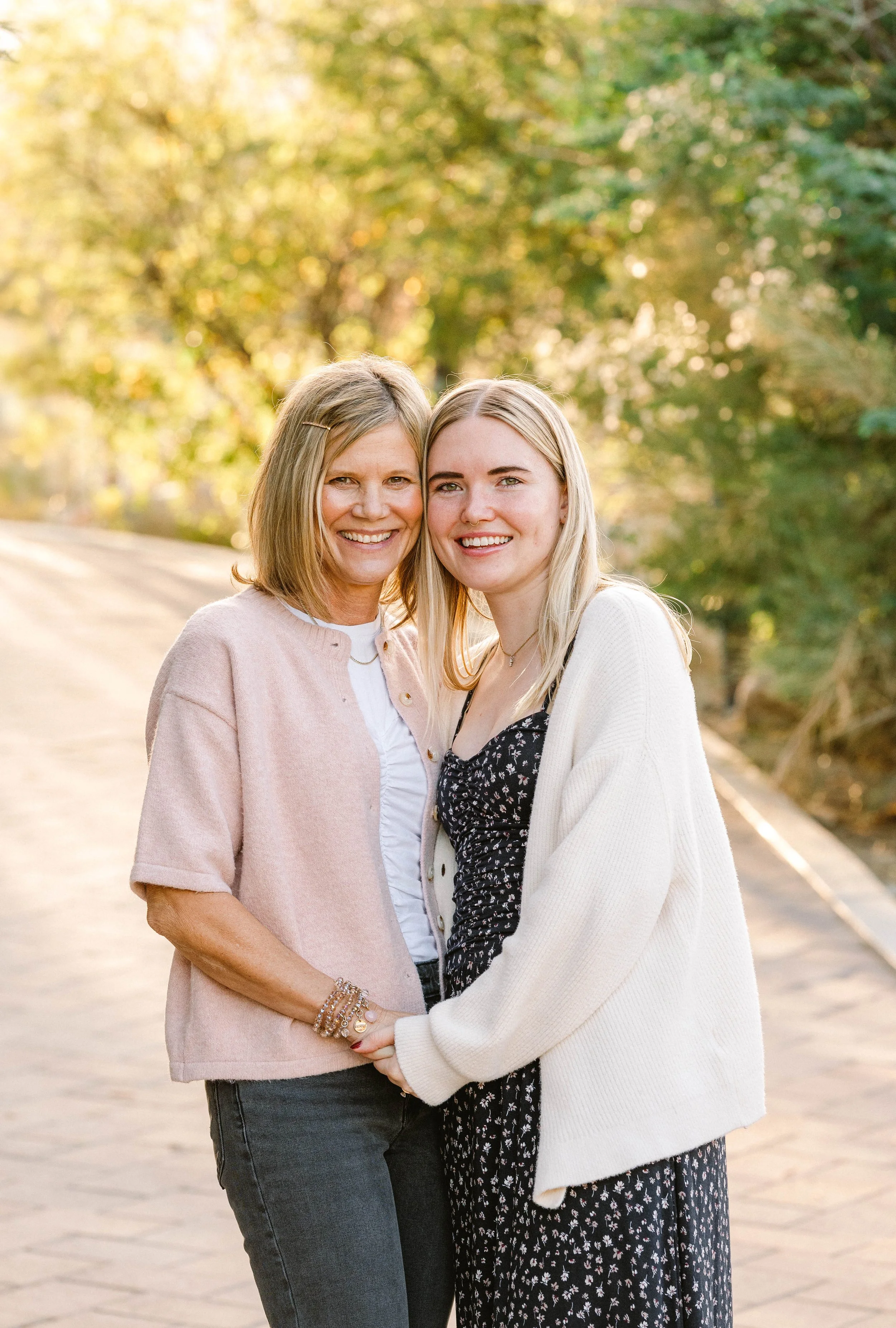 Two women smiling and holding hands outdoors during golden hour, with trees in the background.