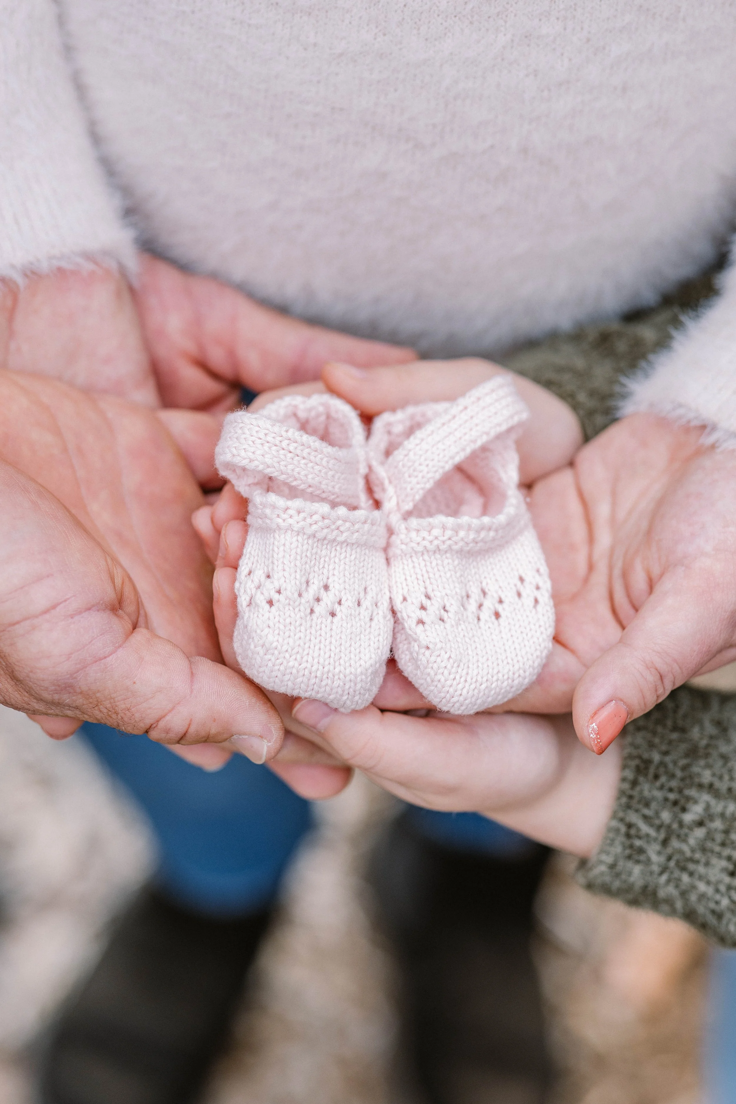 Adult and child holding tiny pink knitted baby shoes.