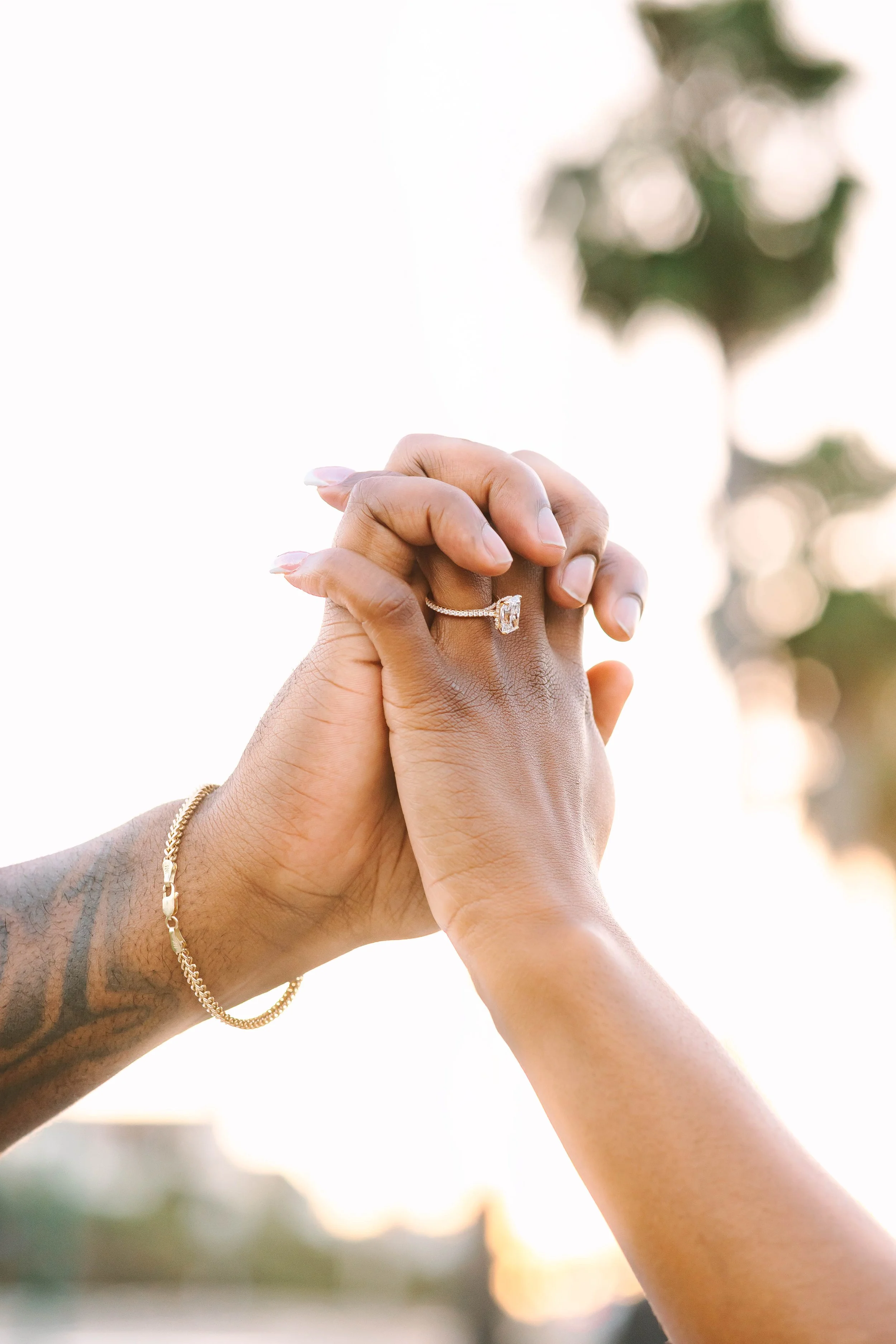 Close up photograph of two hands being held, with engagement ring in focus