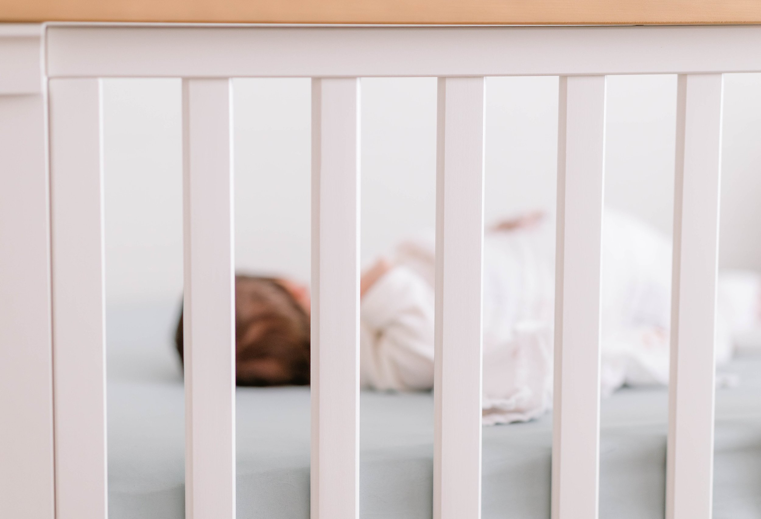 Close-up of a white crib with a sleeping child inside, viewed through the bars.