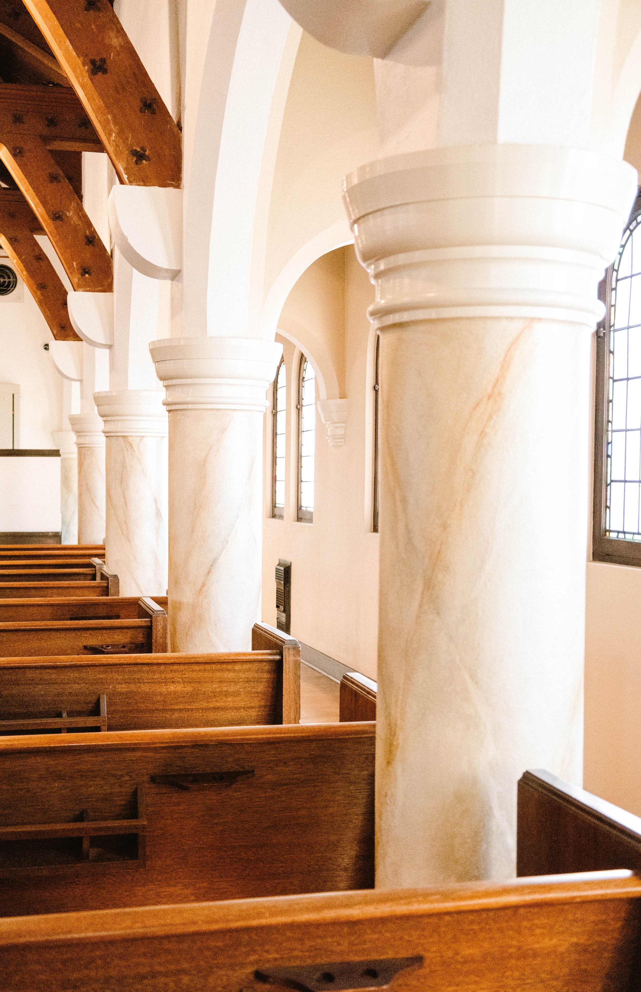 Inside of a church pew area with marble columns, arched ceilings, and stained glass windows.