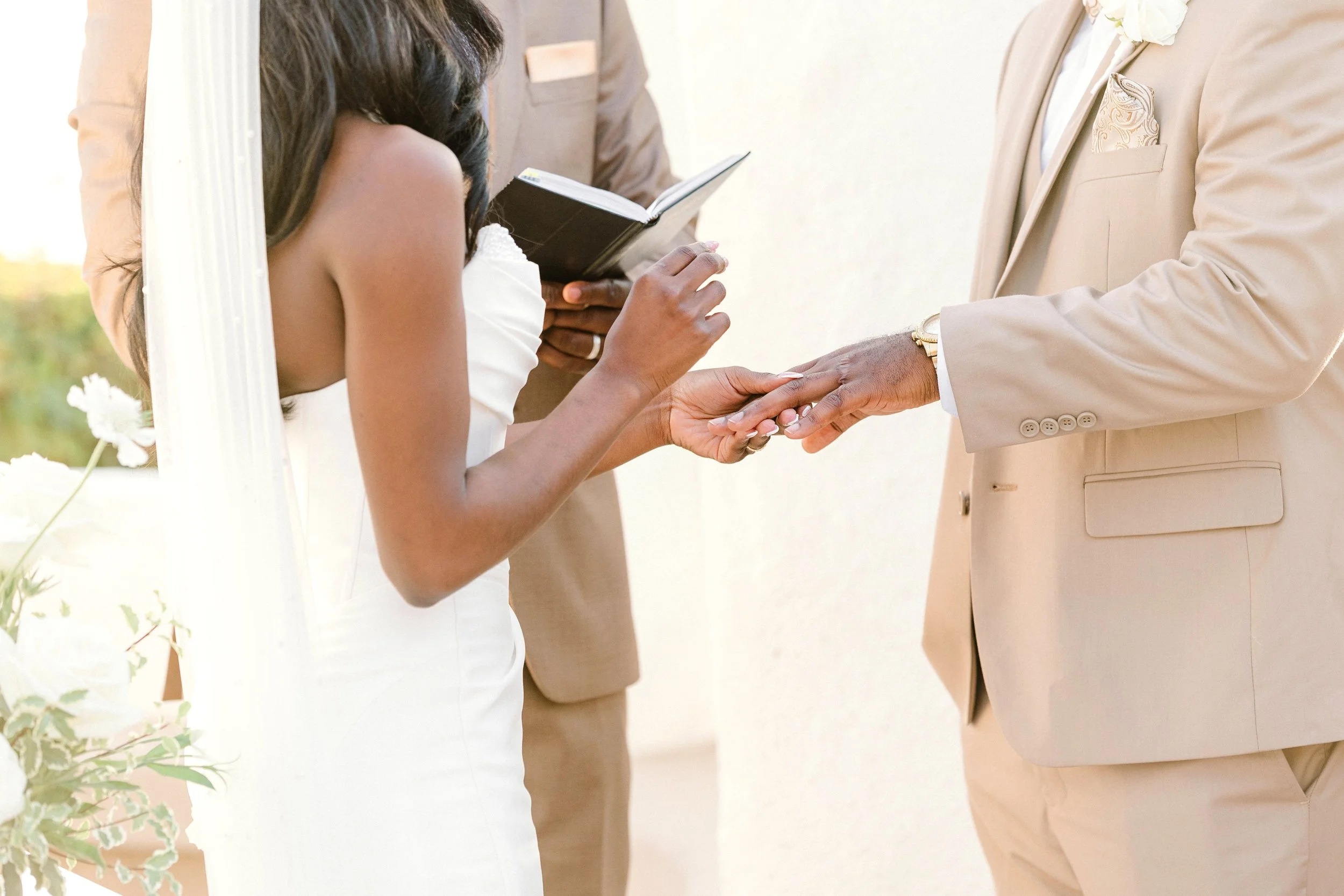 A bride and groom exchange wedding vows and hold hands during their wedding ceremony, with an officiant reading from a book.