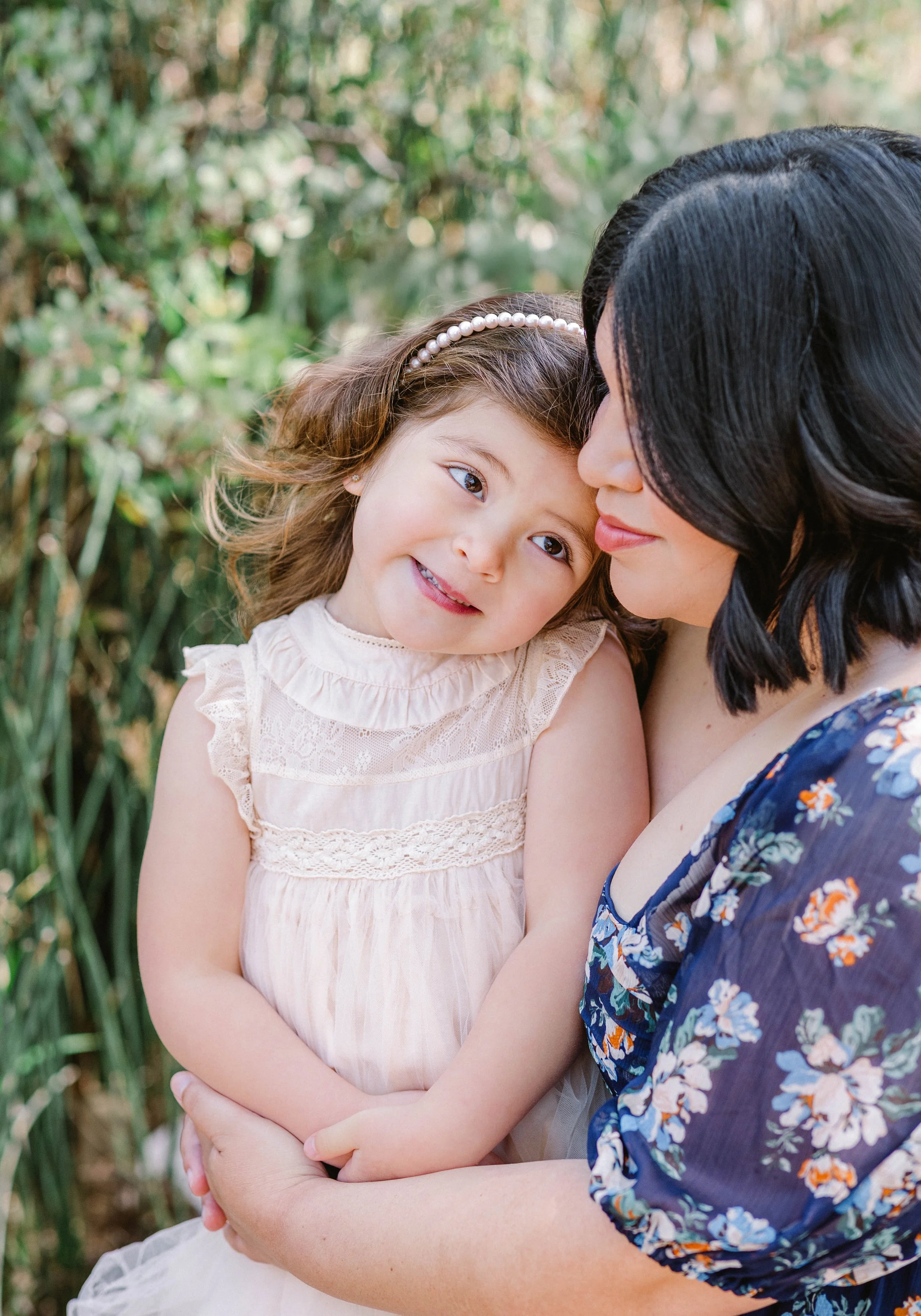A woman holding a young girl in an outdoor setting with greenery in the background.