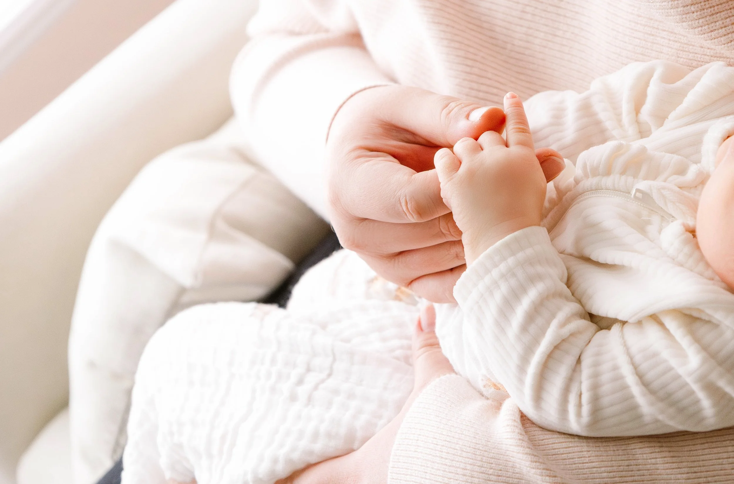 A baby holding an adult's finger, close-up of hands and arms.