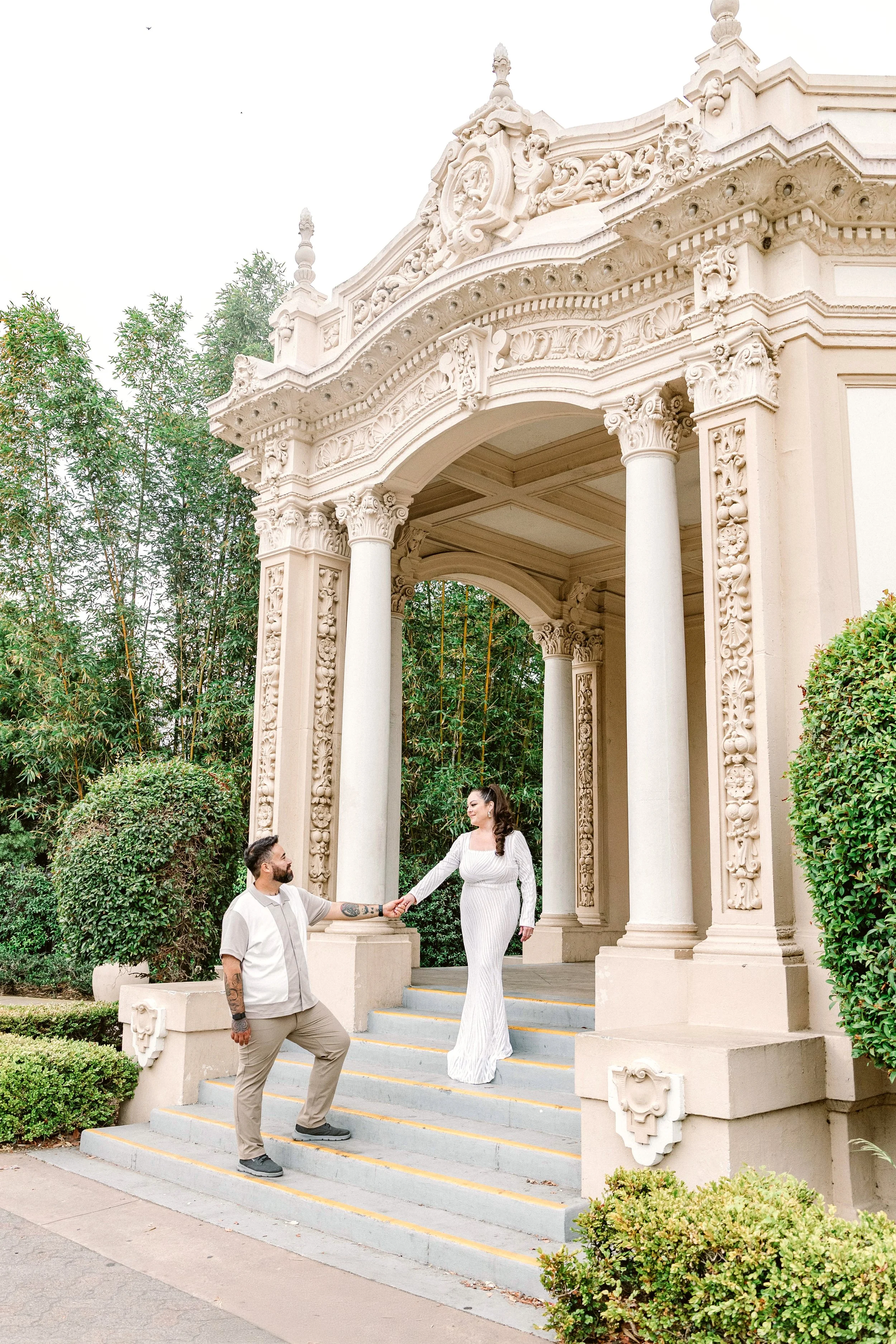 Man leads woman down the stairs under an ornate Spanish style arch in Balboa Park, San Diego