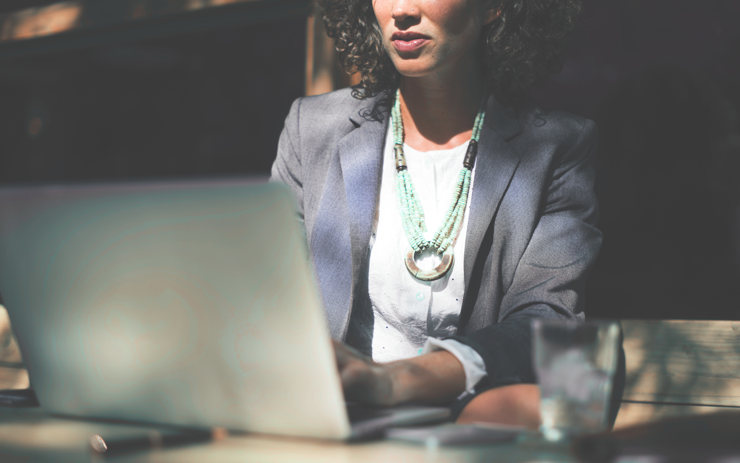 Female business owner wearing blue blazer, white shirt and turquoise necklace attending online therapy.