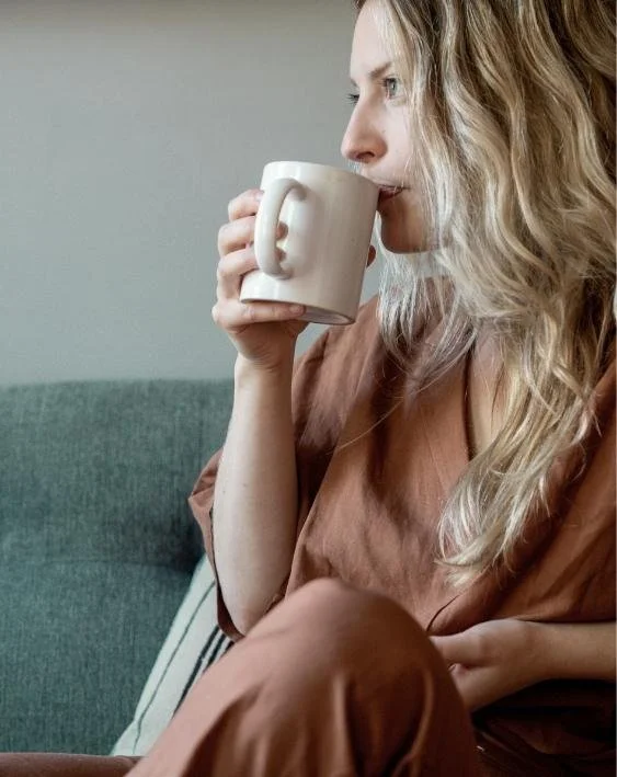 Woman sitting on a couch holding a mug and looking away thoughtfully