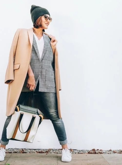 Confident woman with tan coat walking down the sidewalk.