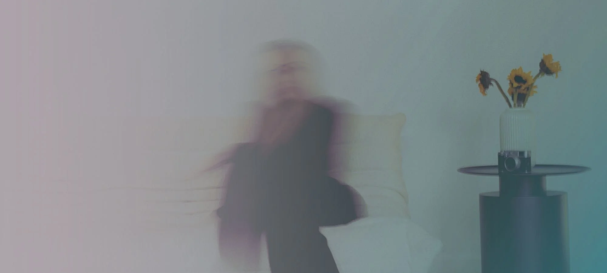 Blurred woman managing stress sitting on a couch in a minimalist room with a side table holding a vase of sunflowers.