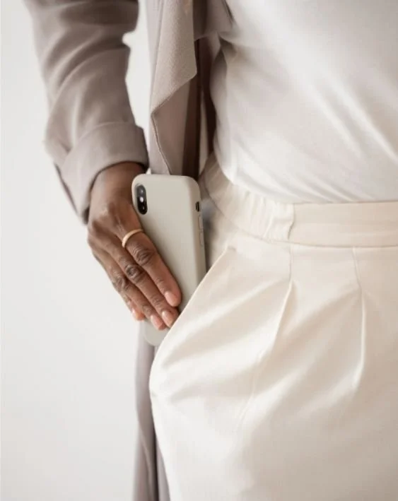 Woman standing in a light neutral outfit holding a phone