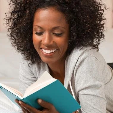 Woman smiling reading book on her bed