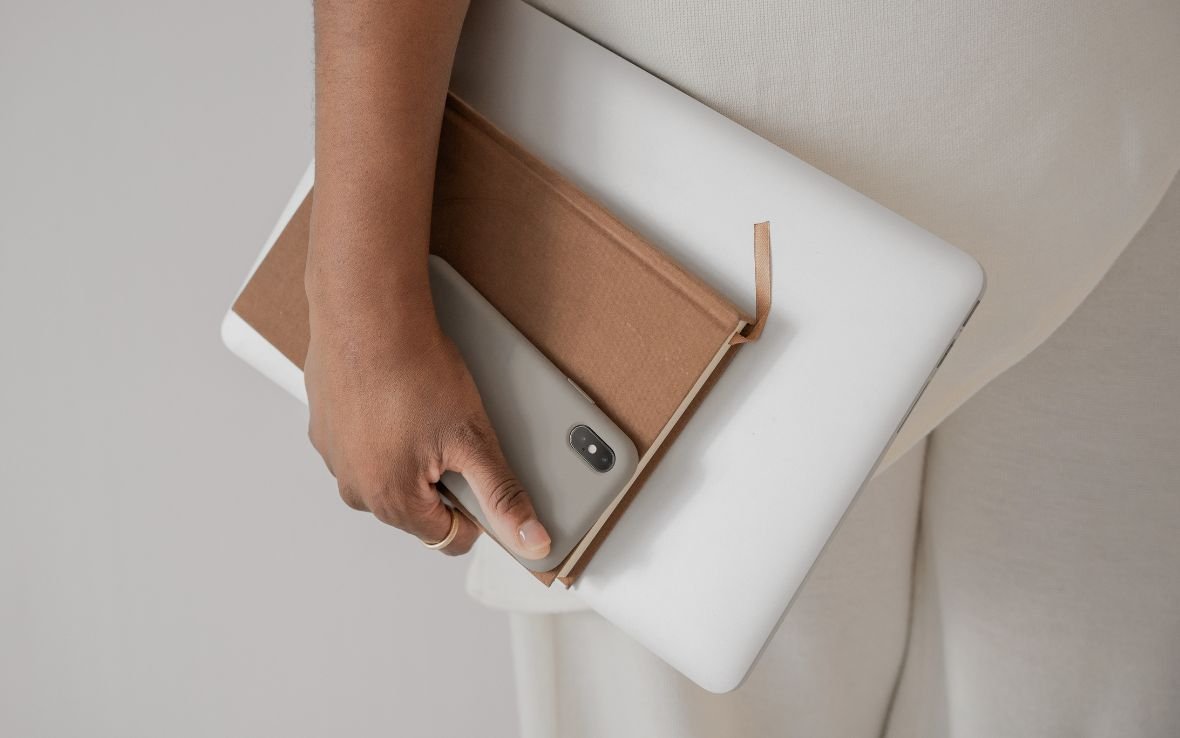 Professional woman in white carrying a laptop, notebook, and phone.