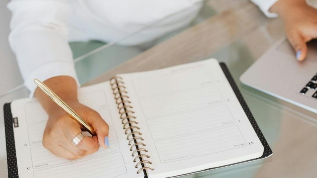 Person writing in an open planner at a desk