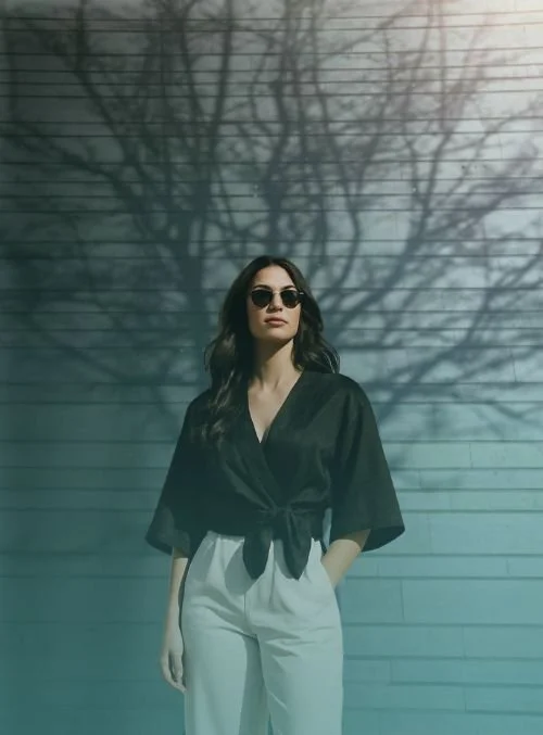 Woman in sunglasses and black wrap top and white pants standing outside with shadow of tree behind her representing growth with imposter syndrome.