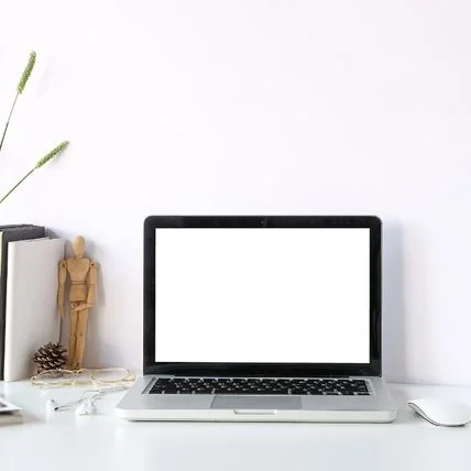 Computer on desk with wooden figure, glasses, and headphones.