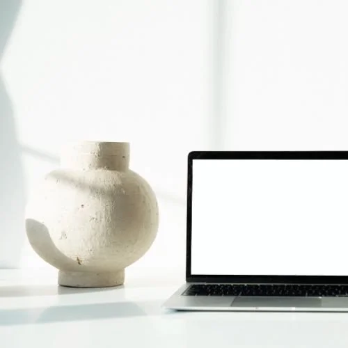 Laptop on white desk with vase on white desk for decor in anxiety therapy office.