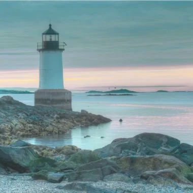 Lighthouse on a rocky Massachusetts coastline at sunrise with calm ocean water