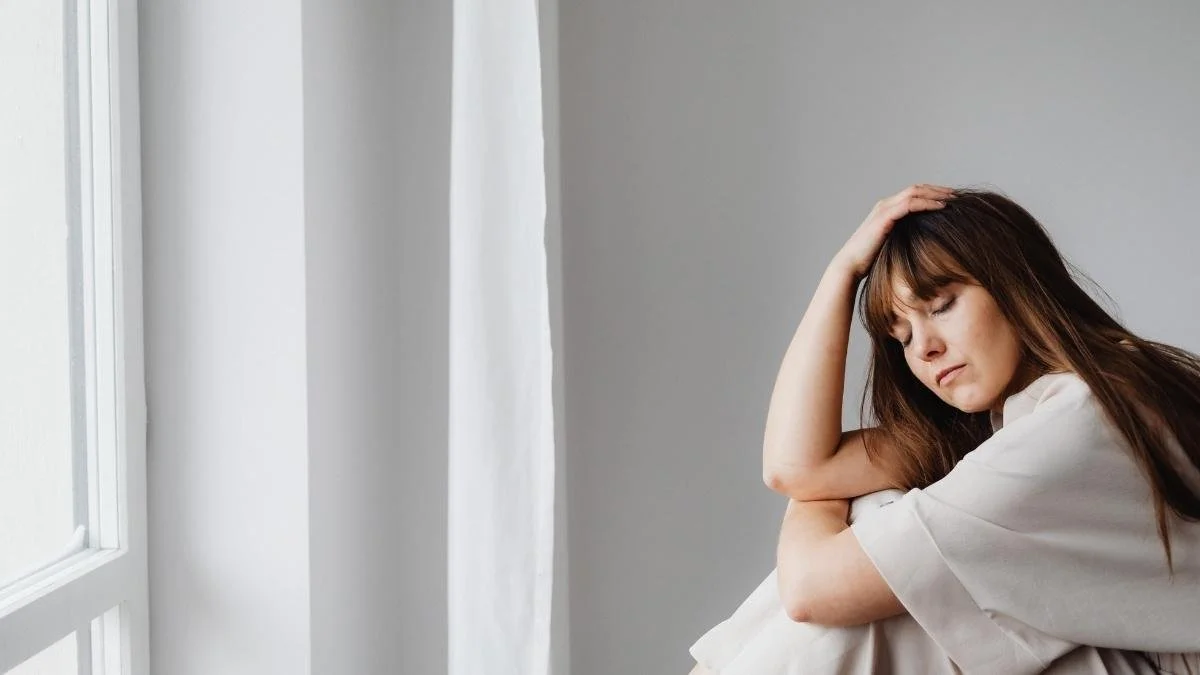 Woman sitting by a window with her hand resting on her head