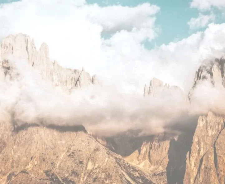 Mountain landscape with rocky peaks, clouds, and a blue sky.