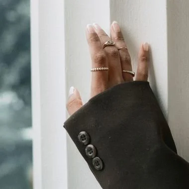 Close-up of a woman's hand resting on a white window frame, wearing rings, with a dark blazer sleeve visible.