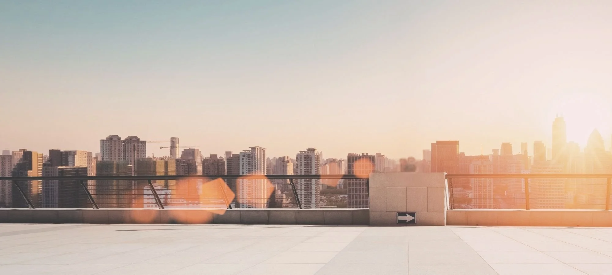 Sunlit city skyline viewed from a rooftop terrace with an open foreground and warm lens flare.