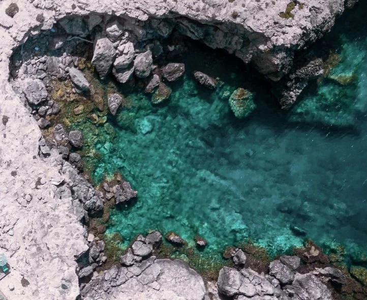 An aerial view of a small, clear blue-green water pool surrounded by rocky terrain representing hard work in perfectionism therapy.