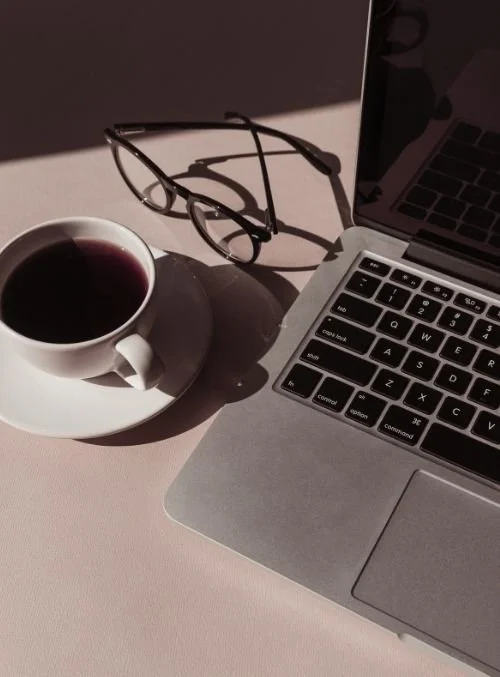 Laptop on white desk with black used for online perfectionism therapy.