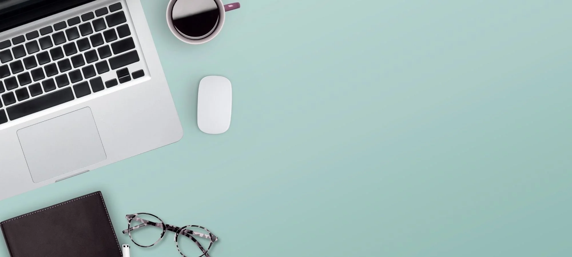 Arial view of teal desk with laptop, coffee, computer mouse, and glasses.