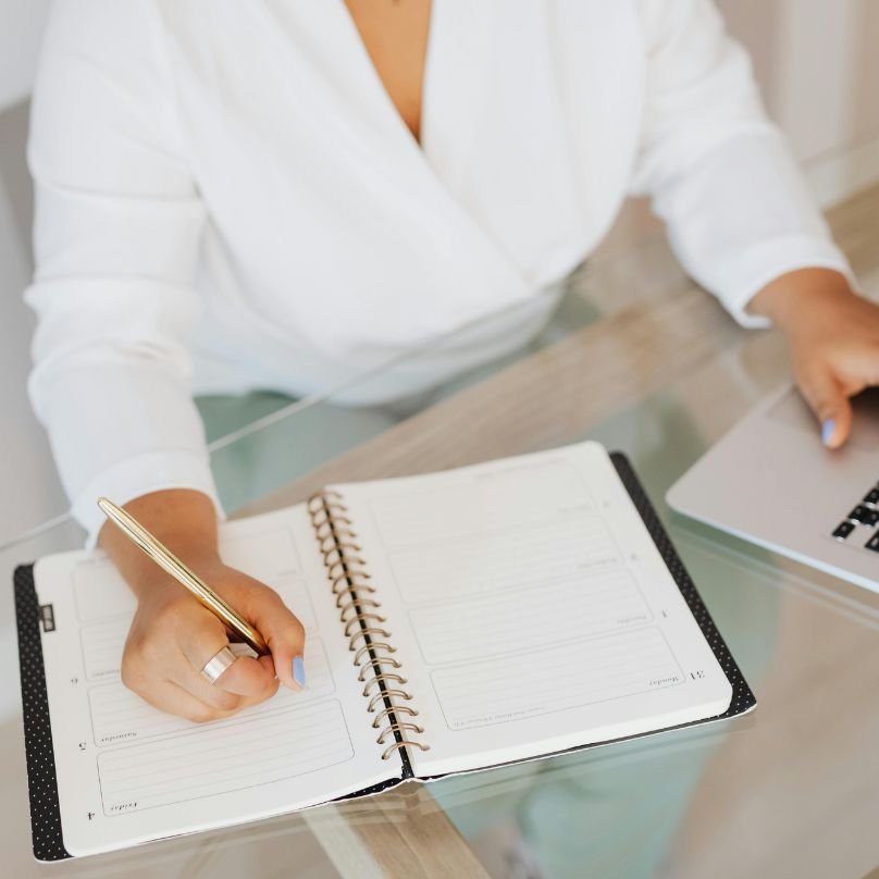 Woman writing in her calendar and on laptop filling out contact form for therapy.