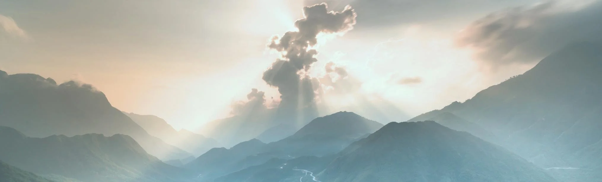Mountains covered in green trees at sunrise with light pink sun coming out of the clouds representing a fresh start with building self-esteem.