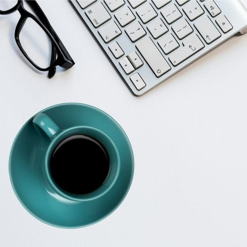 Teal mug and black glasses on white desk with computer keyboard used for online therapy for imposter syndrome.