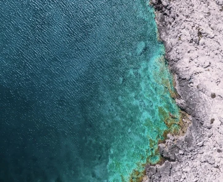 Aerial view of a rocky shoreline with clear, perfect turquoise water.