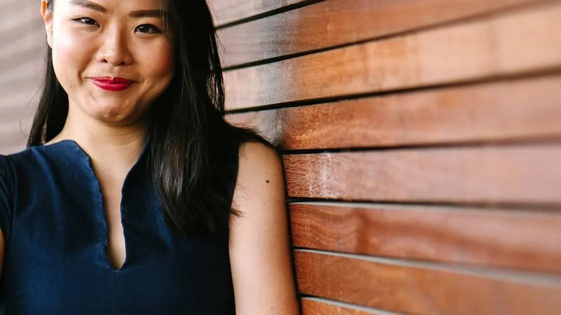 Woman in professional attire leaning against a while with a smile