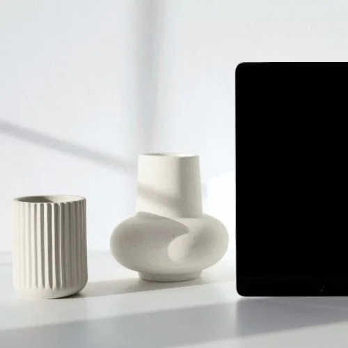 Minimalist desk scene with white ceramic vases and a black tablet in soft natural light.