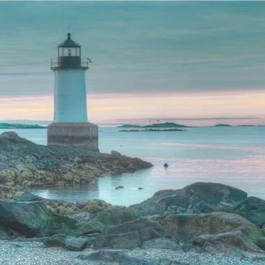 Massachusetts white lighthouse on a rocky shoreline at sunset