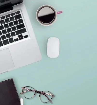 Laptop on light teal desk with mouse and coffee used for online anxiety thearpy