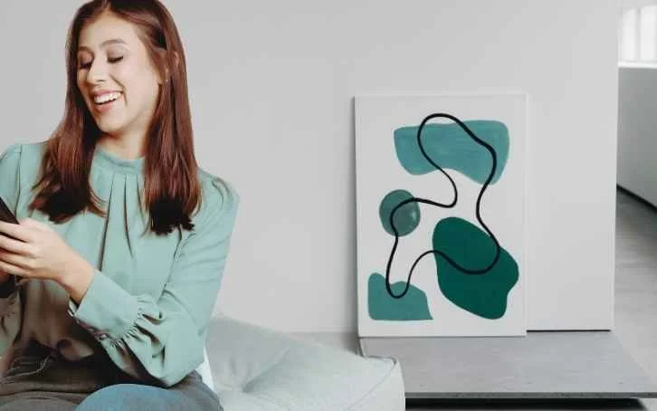 Professional woman in teal blouse laughing and looking relaxed, seated near abstract wall art