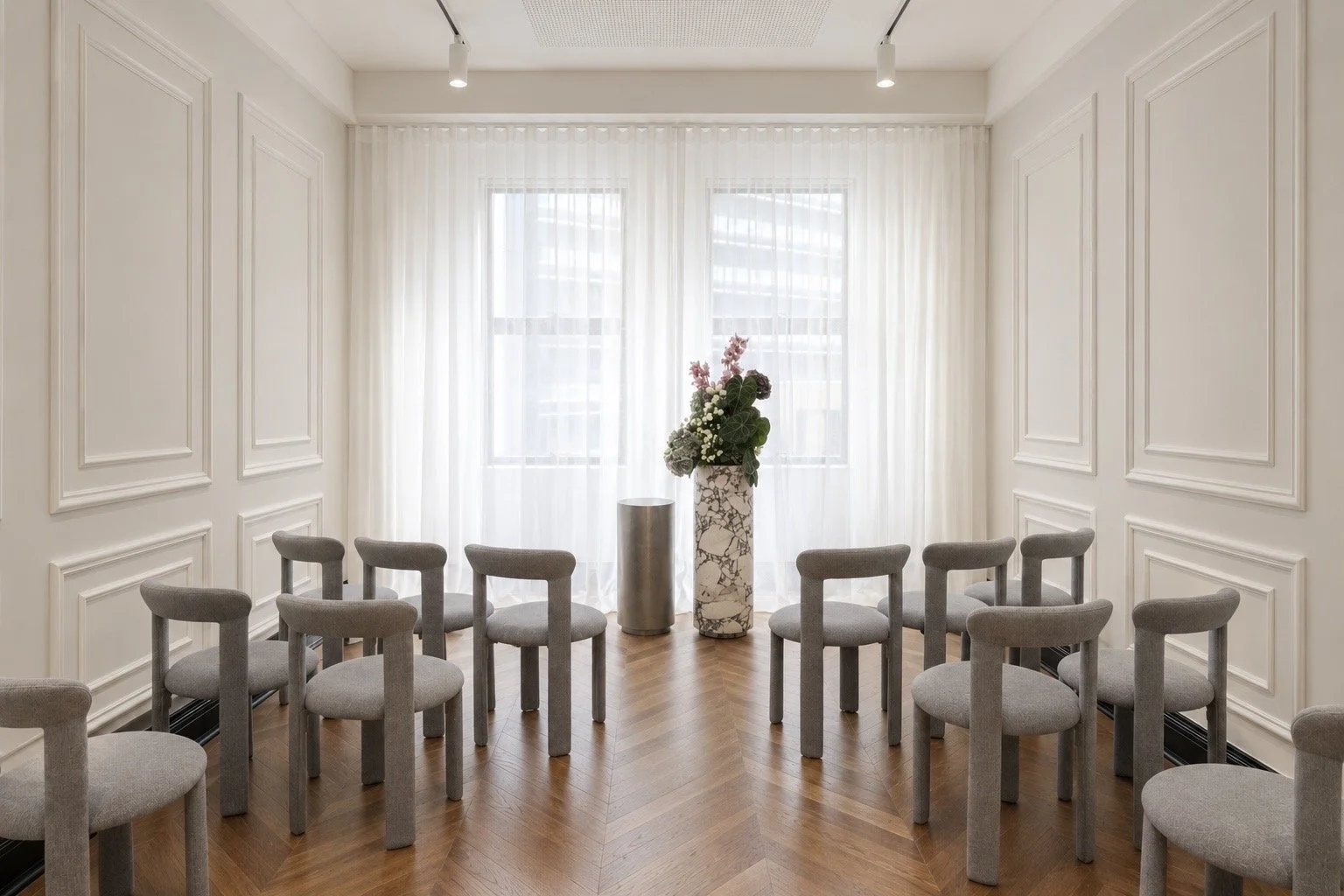 A room styled beautifully with marble plinths, blue upholstered chairs, french wall panelling and parquetry flooring.