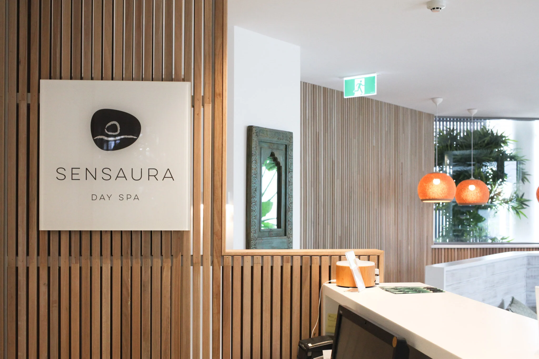 Reception area of SensAURA Day Spa with wooden wall paneling, a sign, and pendant lighting.