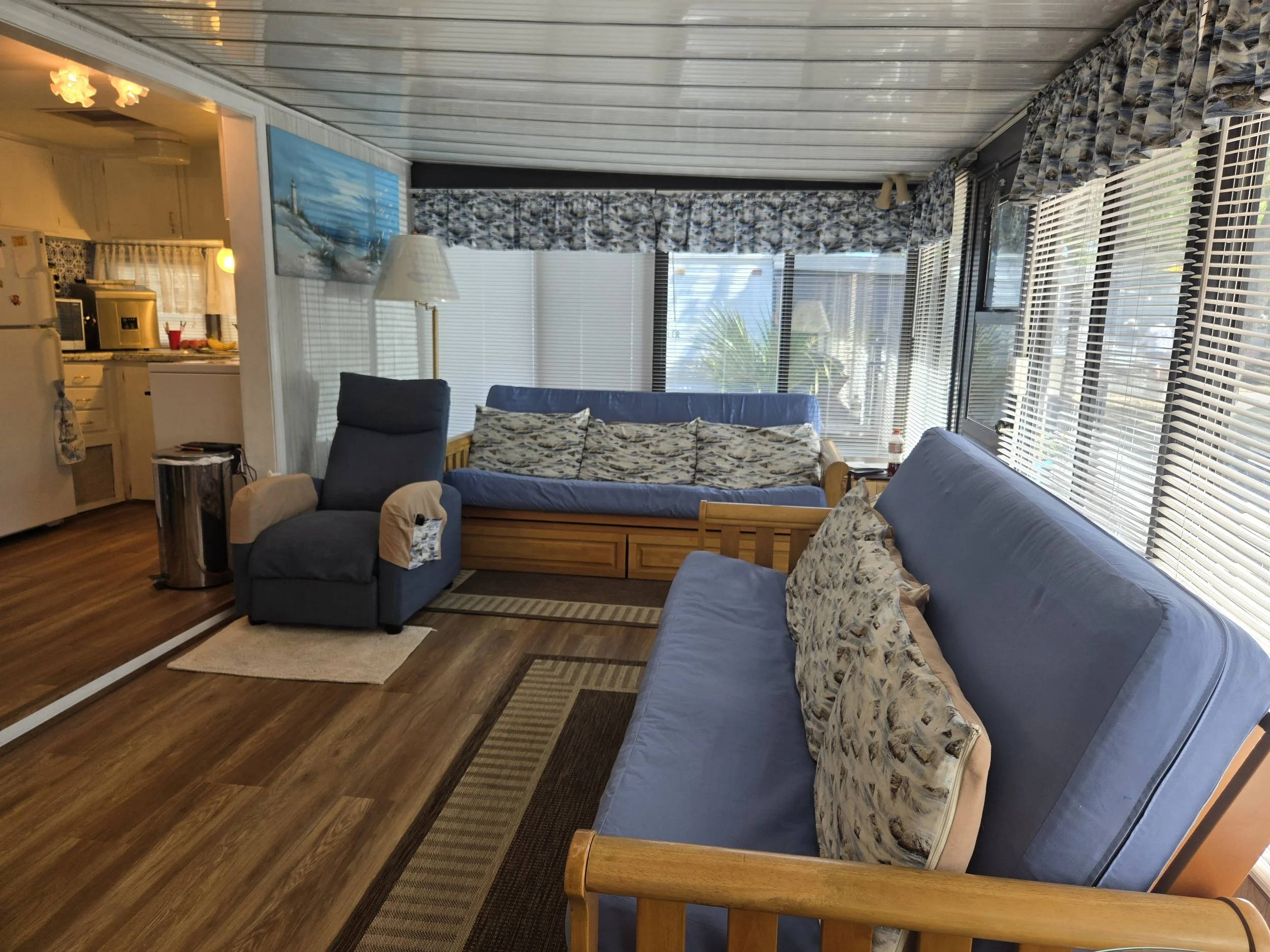 Living room with blue futons, a reclining chair, and large windows with blinds and patterned valances.