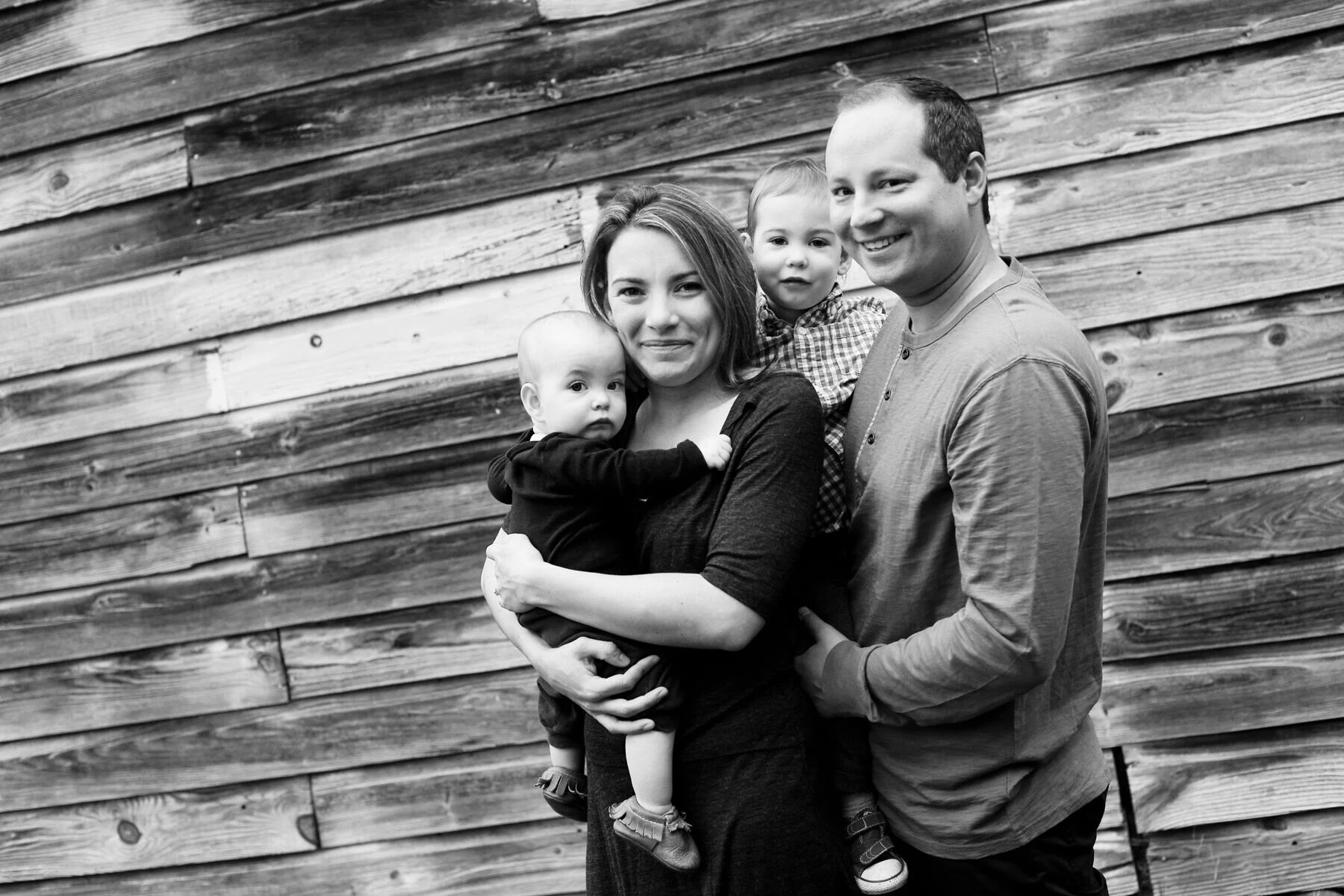 laura standing by a barn with her husband and 2 boys.jpeg