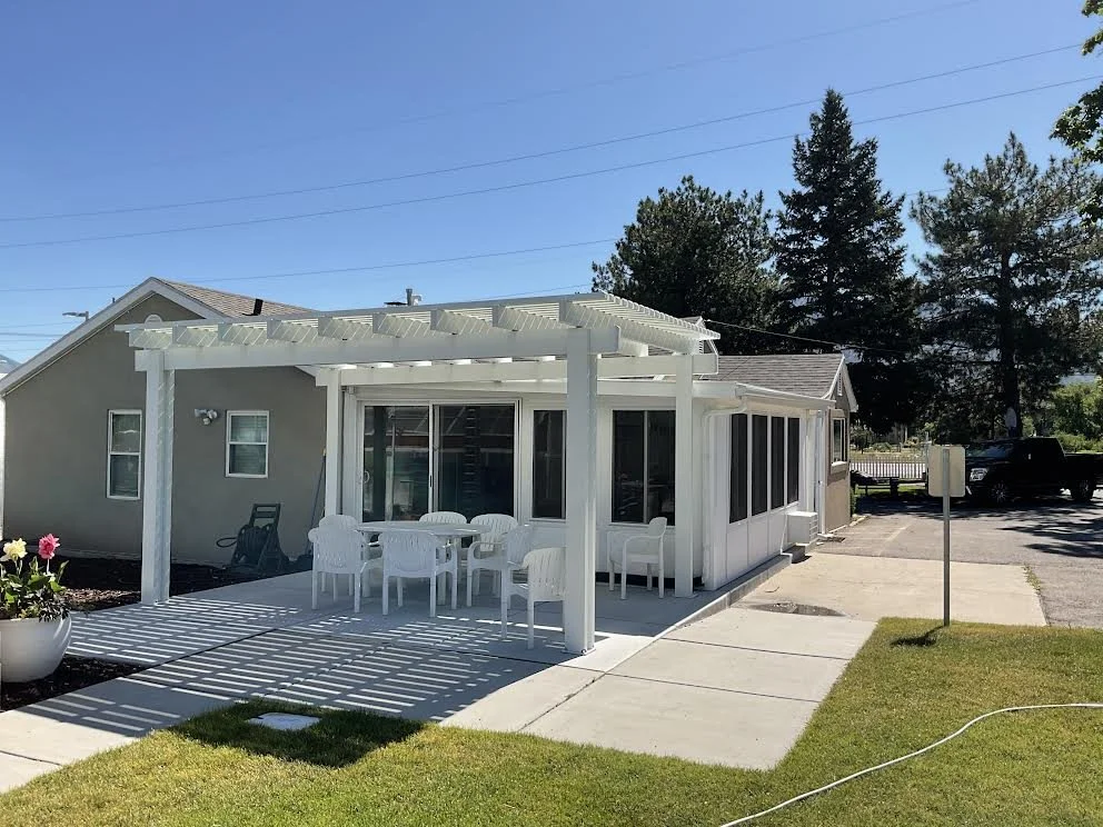White pergola and enclosed patio room attached to a home with outdoor seating and landscaped lawn.