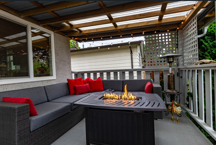 Black wicket patio furniture with red cushions around a fire pit with warm lights in the background