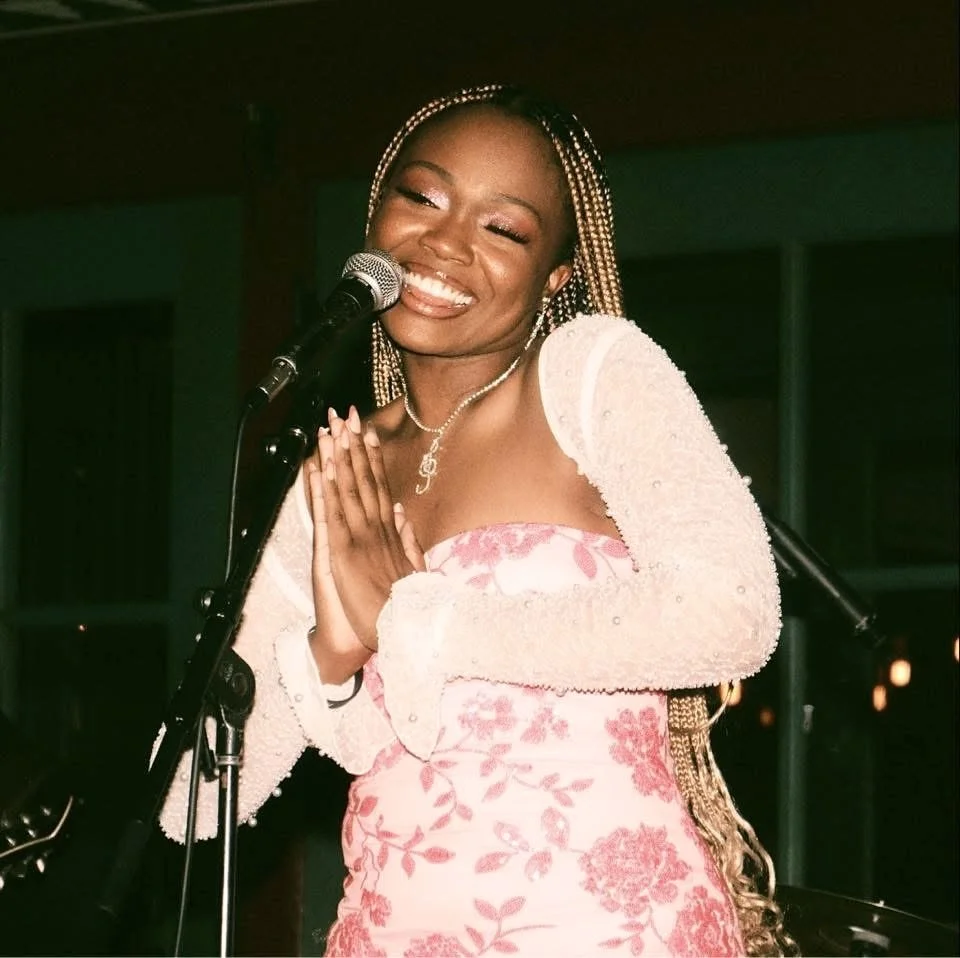 Chloé V smiling in front of a microphone with a pink dress with pink sequined flowers on it and a white sheer long sleeve cropped jacket with pearls on it at the House of Blues New Orleans Voodoo Garden