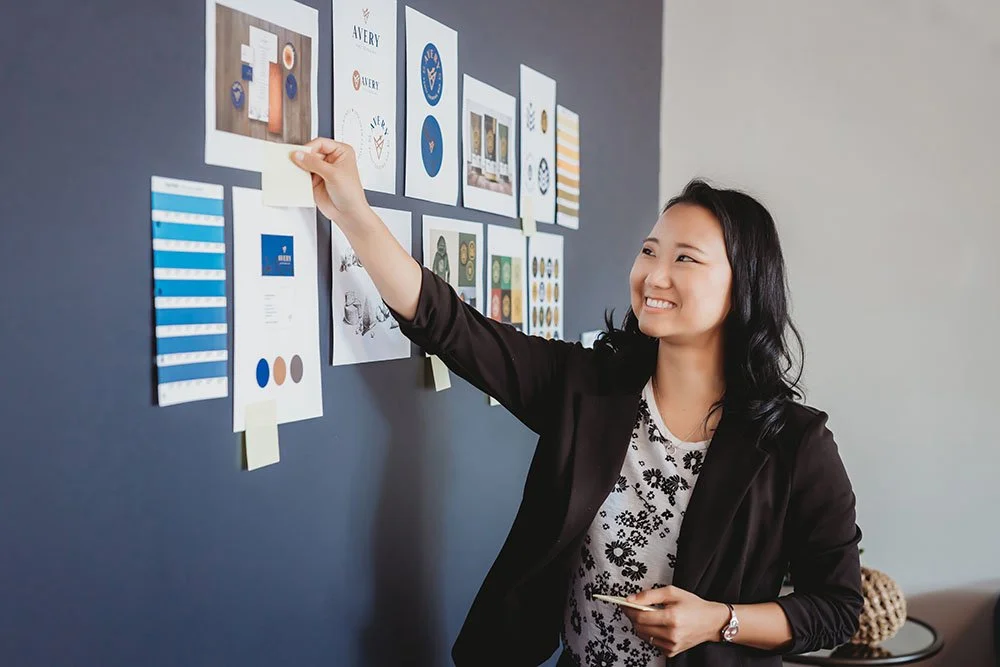 A woman attaching a note to a bulletin board with various images pinned to it.