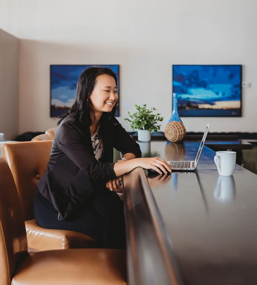 A woman sitting at a table using a laptop, in a modern co-working office space.